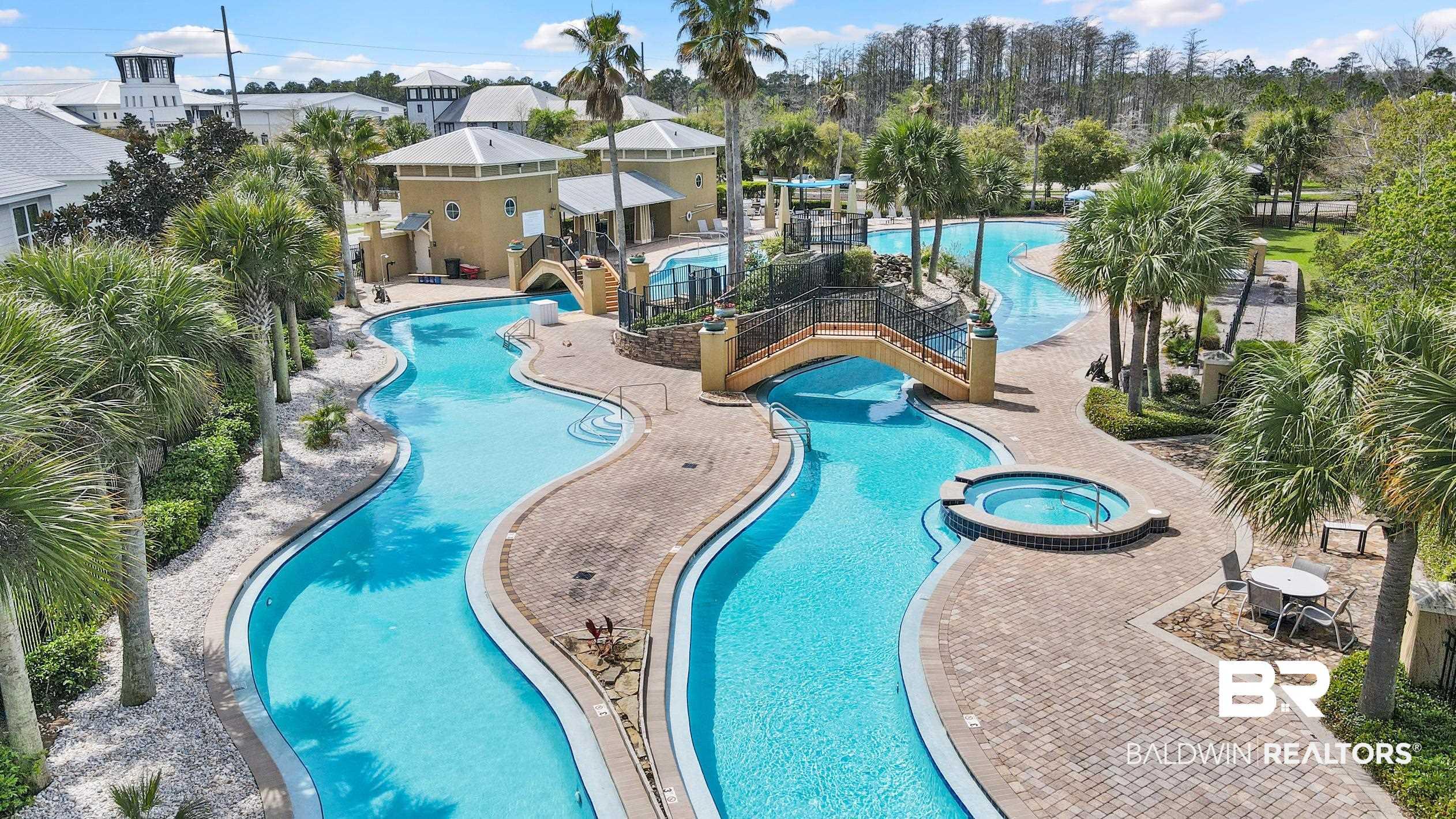 Image 4: Expansive community pool area featuring a lazy river, integrated spa, multiple bridges, and surrounding palm trees