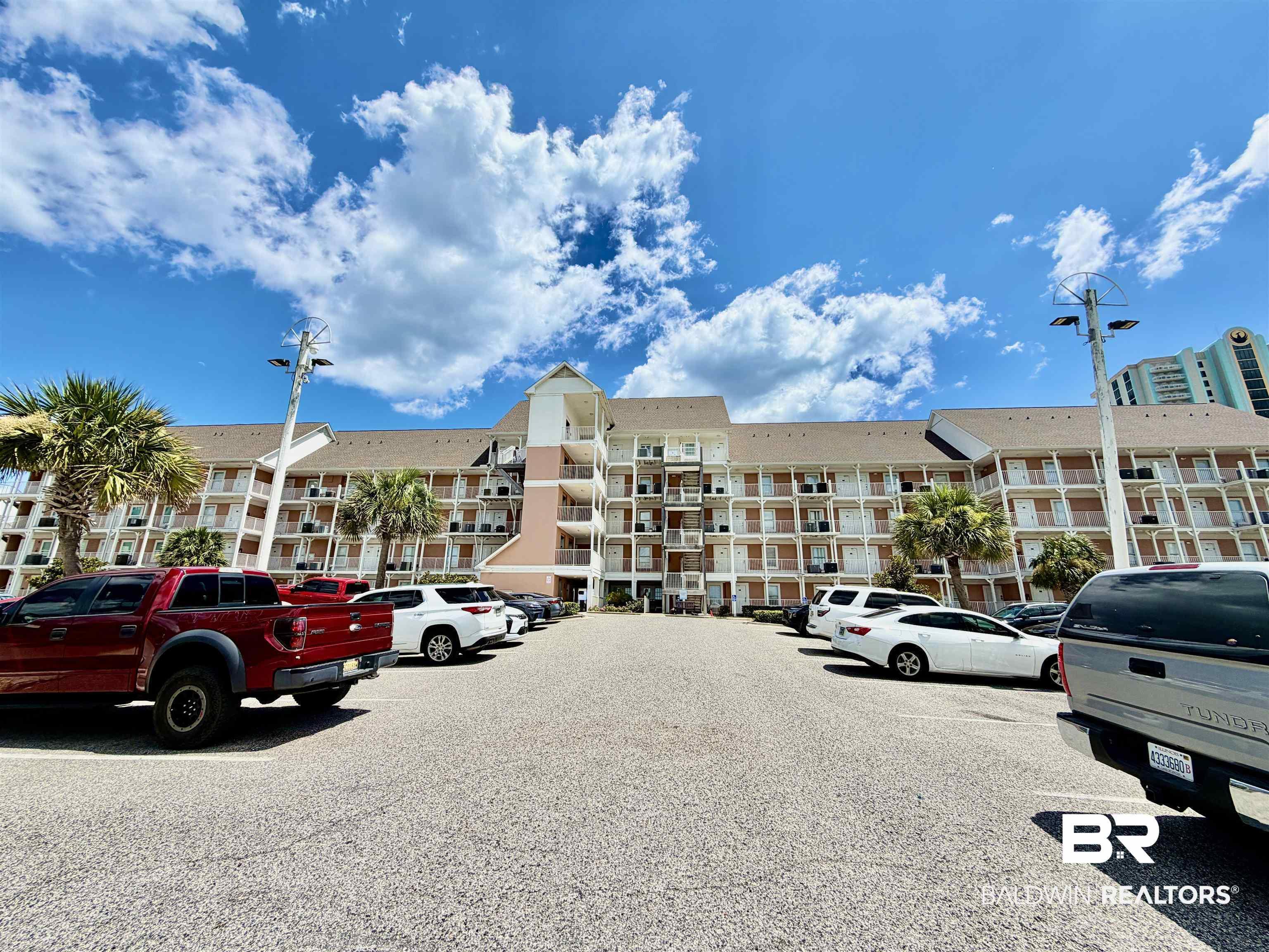 Image 2: Multi-story building featuring individual balconies, a central entrance tower, and mature palm trees