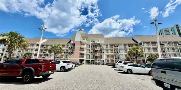 Image 2: Multi-story building featuring individual balconies, a central entrance tower, and mature palm trees