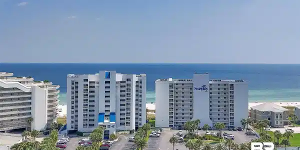 Image 2: Coastal high-rise residences featuring private balconies, ample parking, palm tree landscaping, and direct access to a white sand beach and the Gulf of Mexico