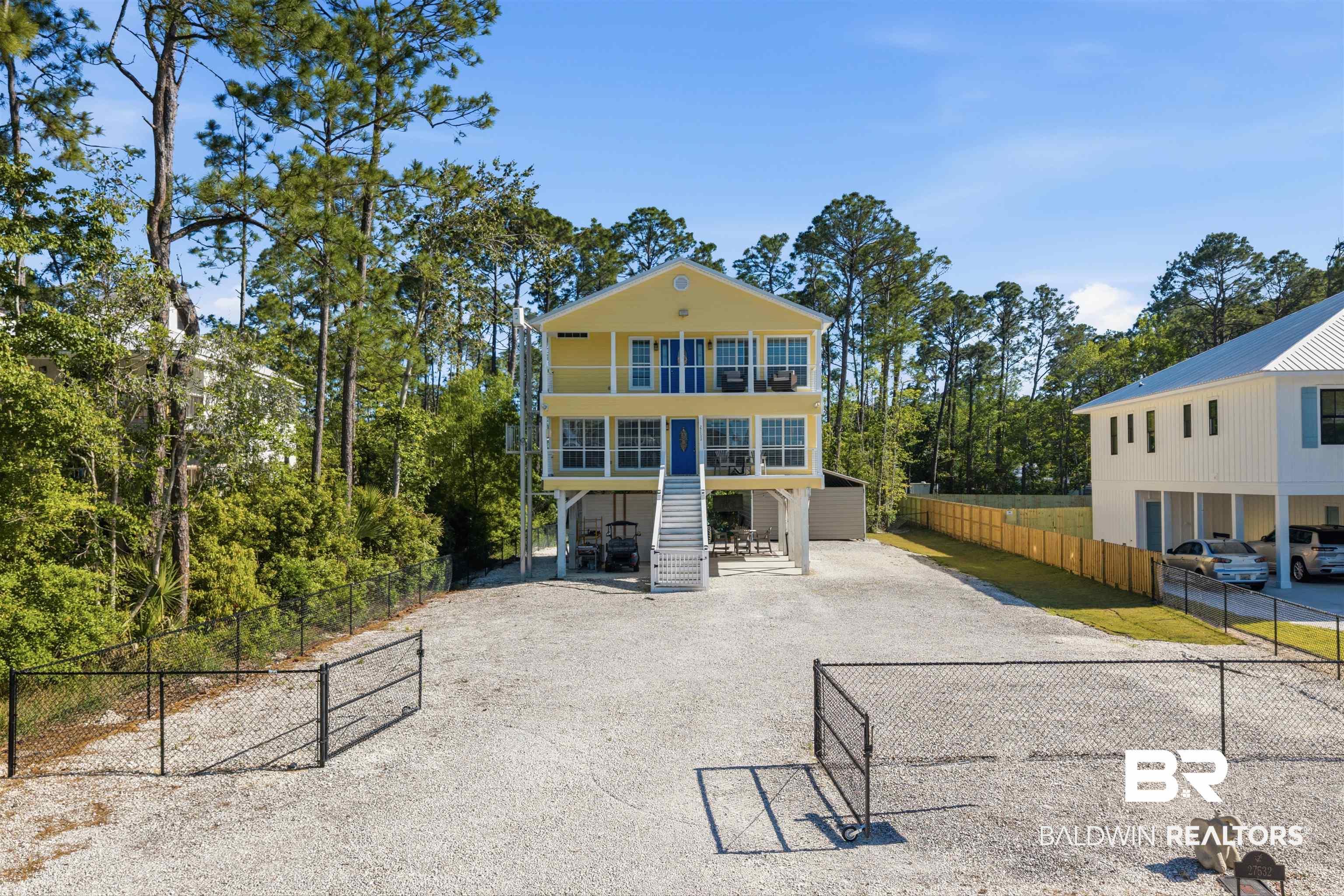 Image 3: View of front of home with gravel driveway, a balcony, and view of wooded area