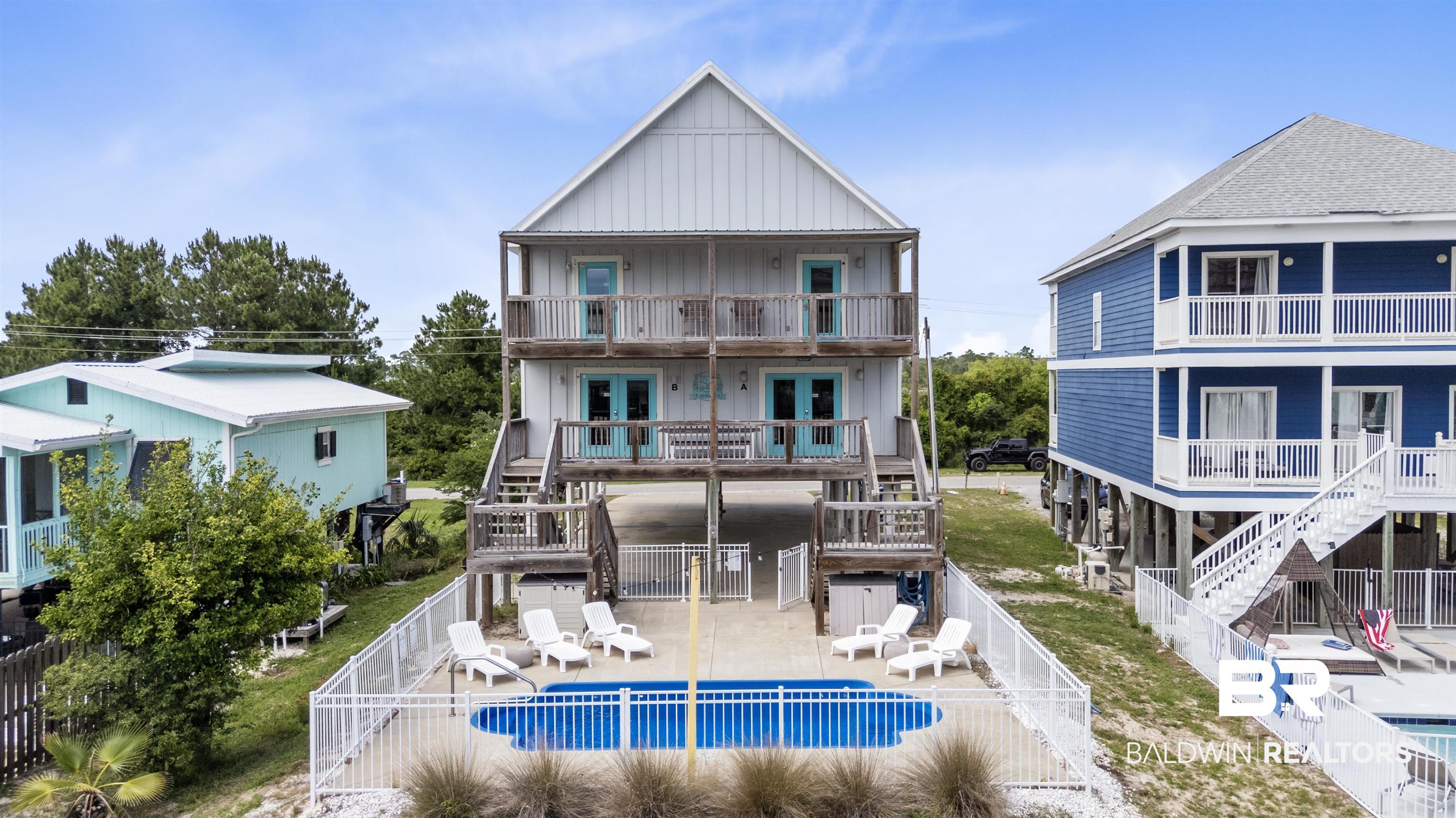 Image 3: Elevated residence featuring a fenced in-ground pool, two levels of covered balconies with teal doors, a gable roof, and wood decking