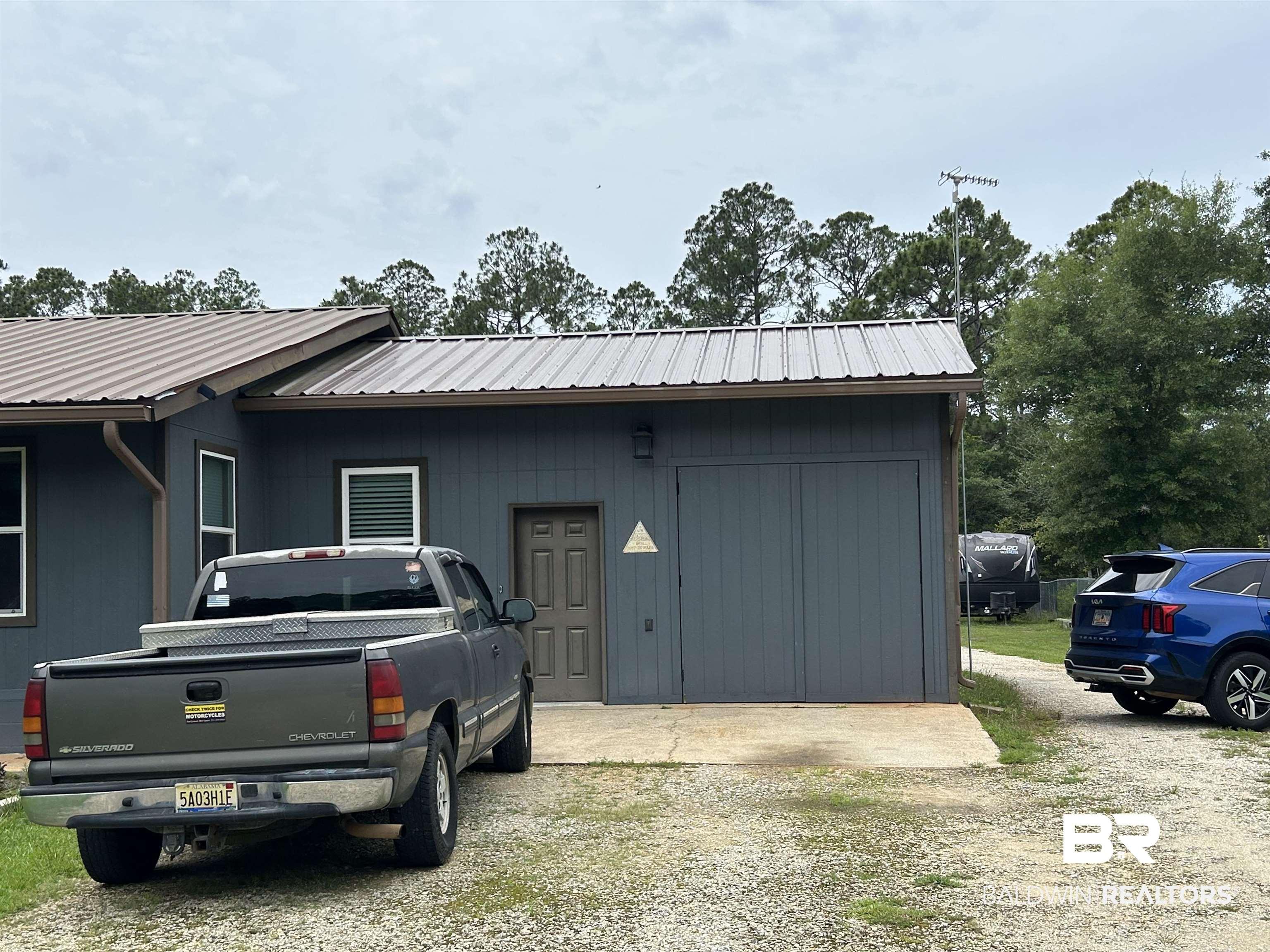 Image 2: Exterior featuring a gray metal roof, vertical siding, and a pull-down garage door