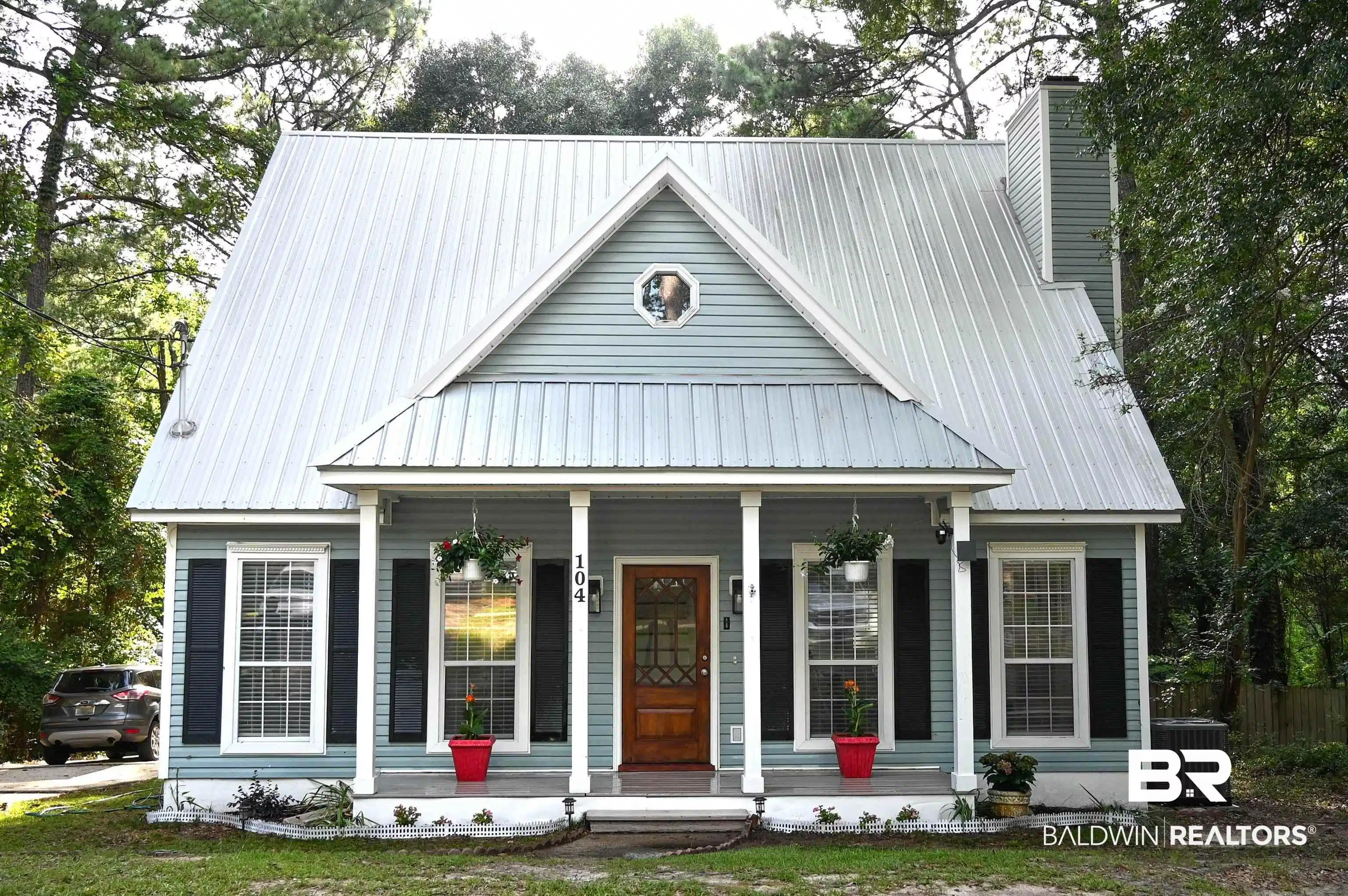 Image 1: Light blue siding exterior featuring a metal roof, front porch with white columns, dark wood-finish front door with glass panels, and black window shutters