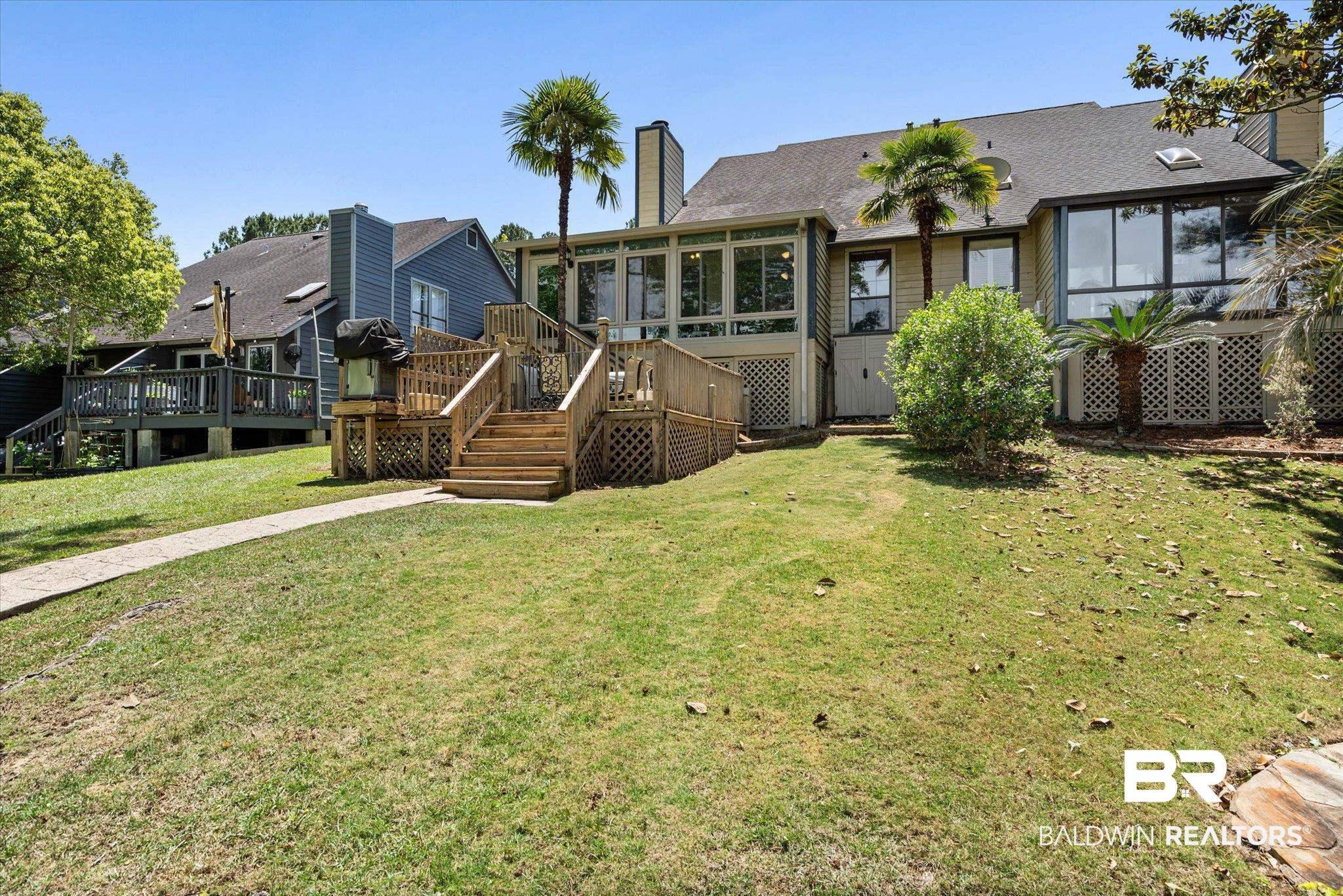 Image 3: Expansive green lawn with a stone pathway, leading to a multi-level wood deck and a sunroom with large windows
