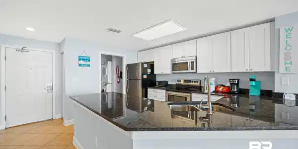 Image 4: Kitchen featuring a peninsula with integrated sink and faucet, dark stone countertops, white upper and lower cabinetry, and stainless steel appliances