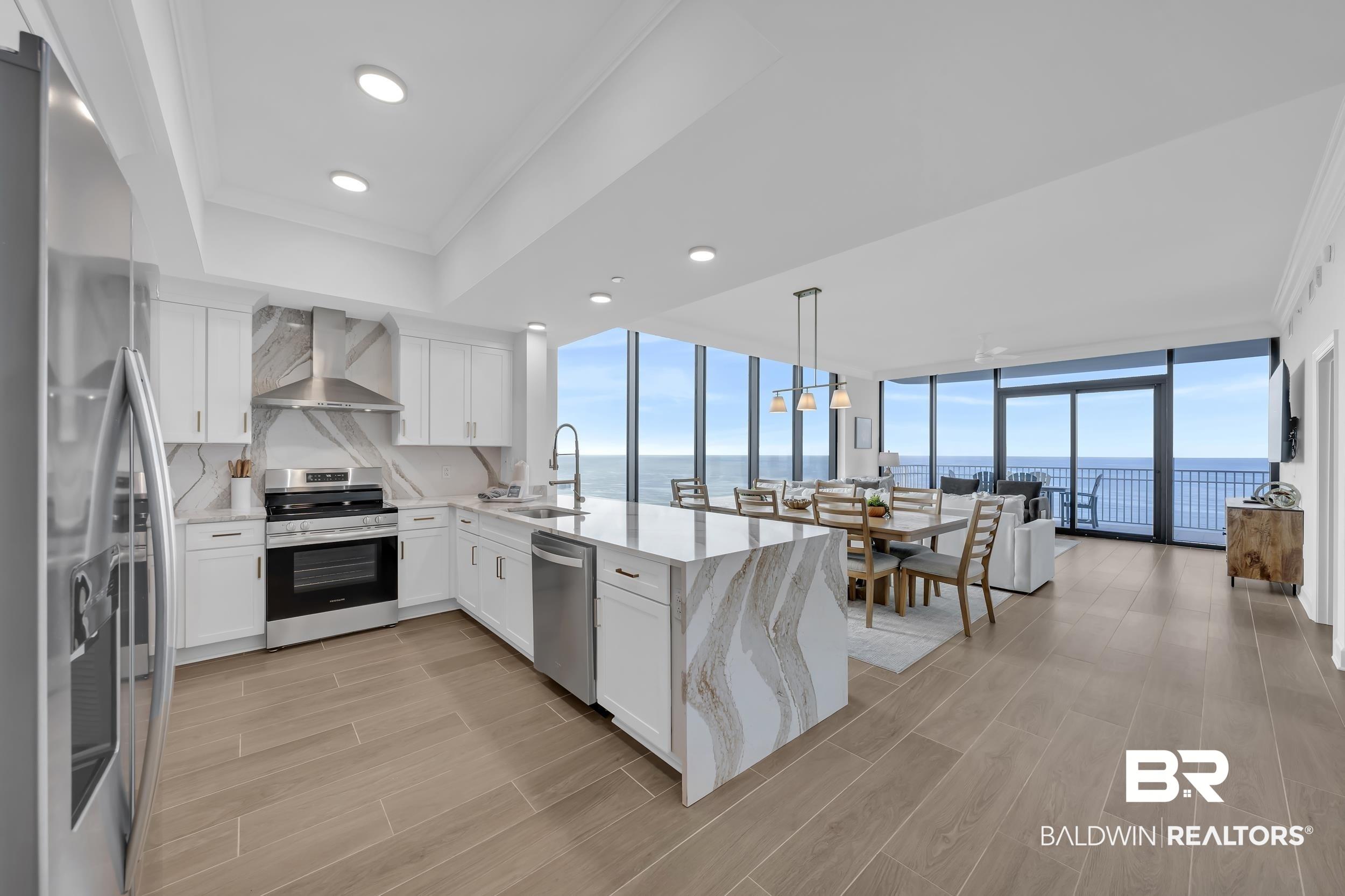 Image 2: Gourmet kitchen with stainless steel appliances, custom white cabinetry, and a large center island featuring a waterfall-edge countertop