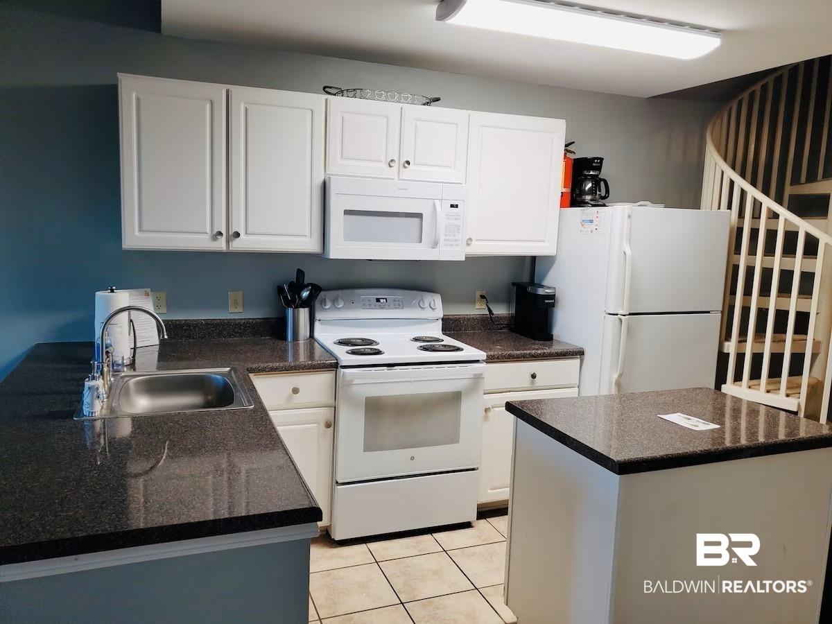 Image 2: Kitchen featuring white appliances, light tile patterned floors, and white cabinetry