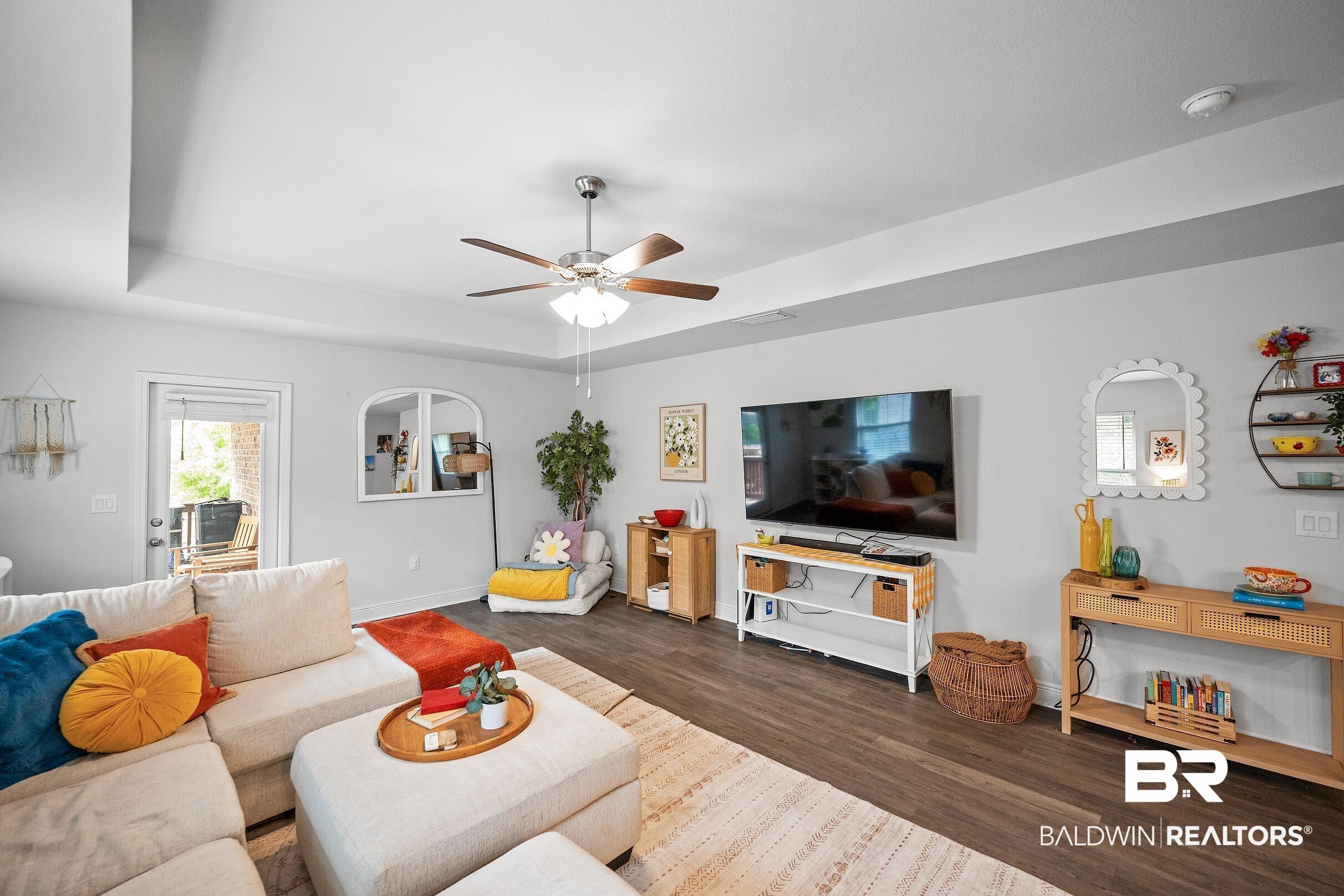 Image 3: Living area featuring dark wood-style flooring, ceiling fan, and a tray ceiling