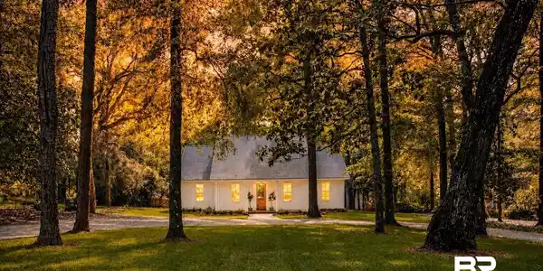 Image 4: White exterior with a light gray roof, set amidst mature trees