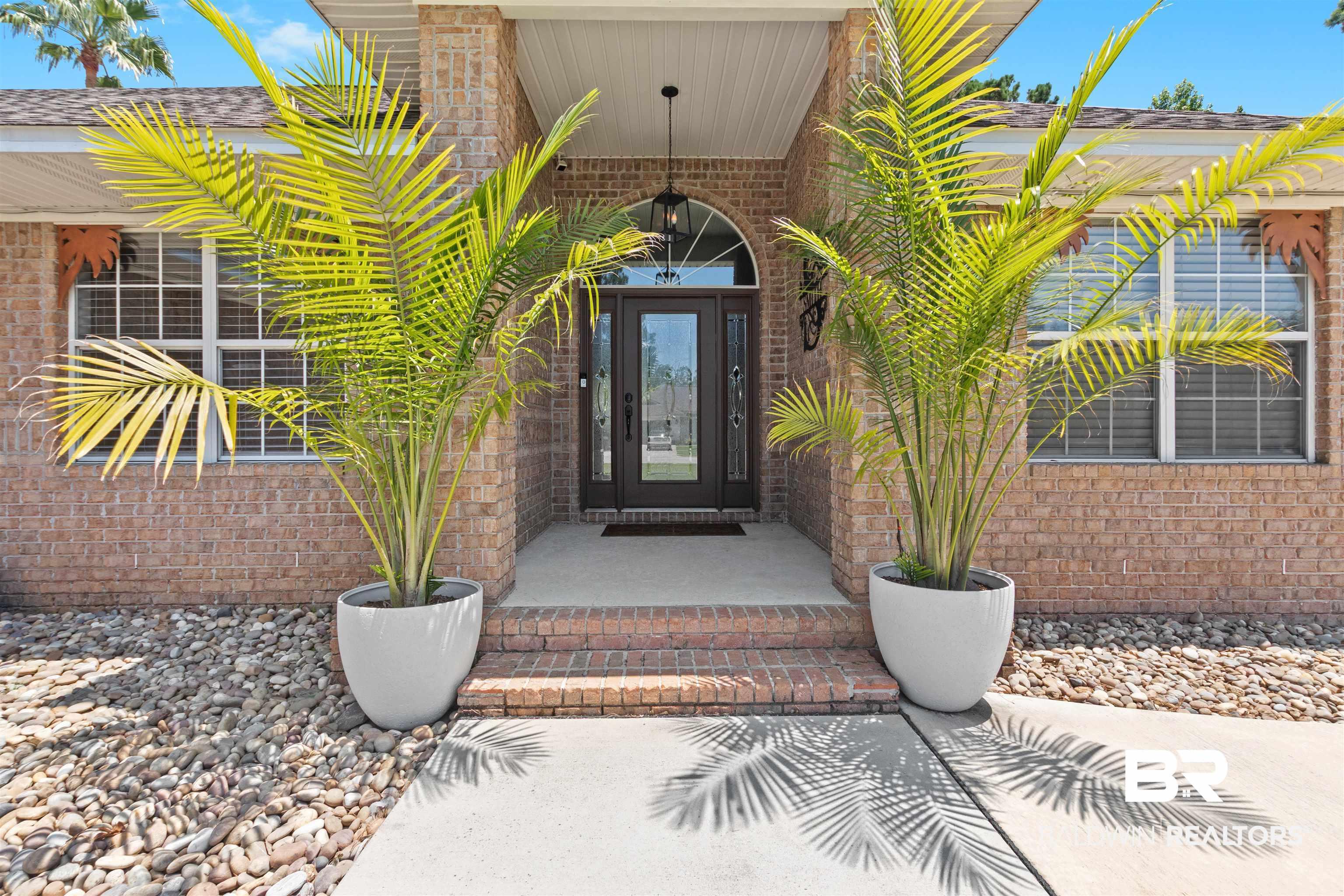 Image 4: Brick-clad exterior featuring a covered entry, arched transom window, dark paneled front door, and symmetrical potted palms