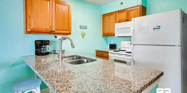Image 2: Kitchen with a peninsula, white appliances, light stone countertops, a kitchen breakfast bar, and brown cabinetry