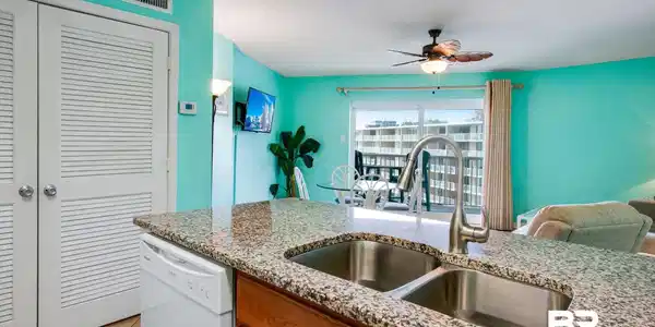 Image 3: Kitchen featuring brown cabinetry, white dishwasher, a textured ceiling, light stone countertops, and light tile patterned floors