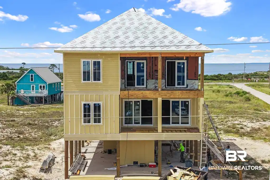 Image 1: Three-story coastal residence featuring a partially installed yellow siding exterior and multiple windows