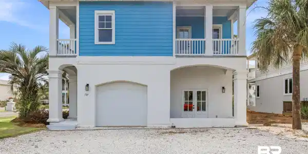 Image 2: Two-story coastal-inspired home featuring a prominent upper balcony, ground-level covered patio, and attached garage