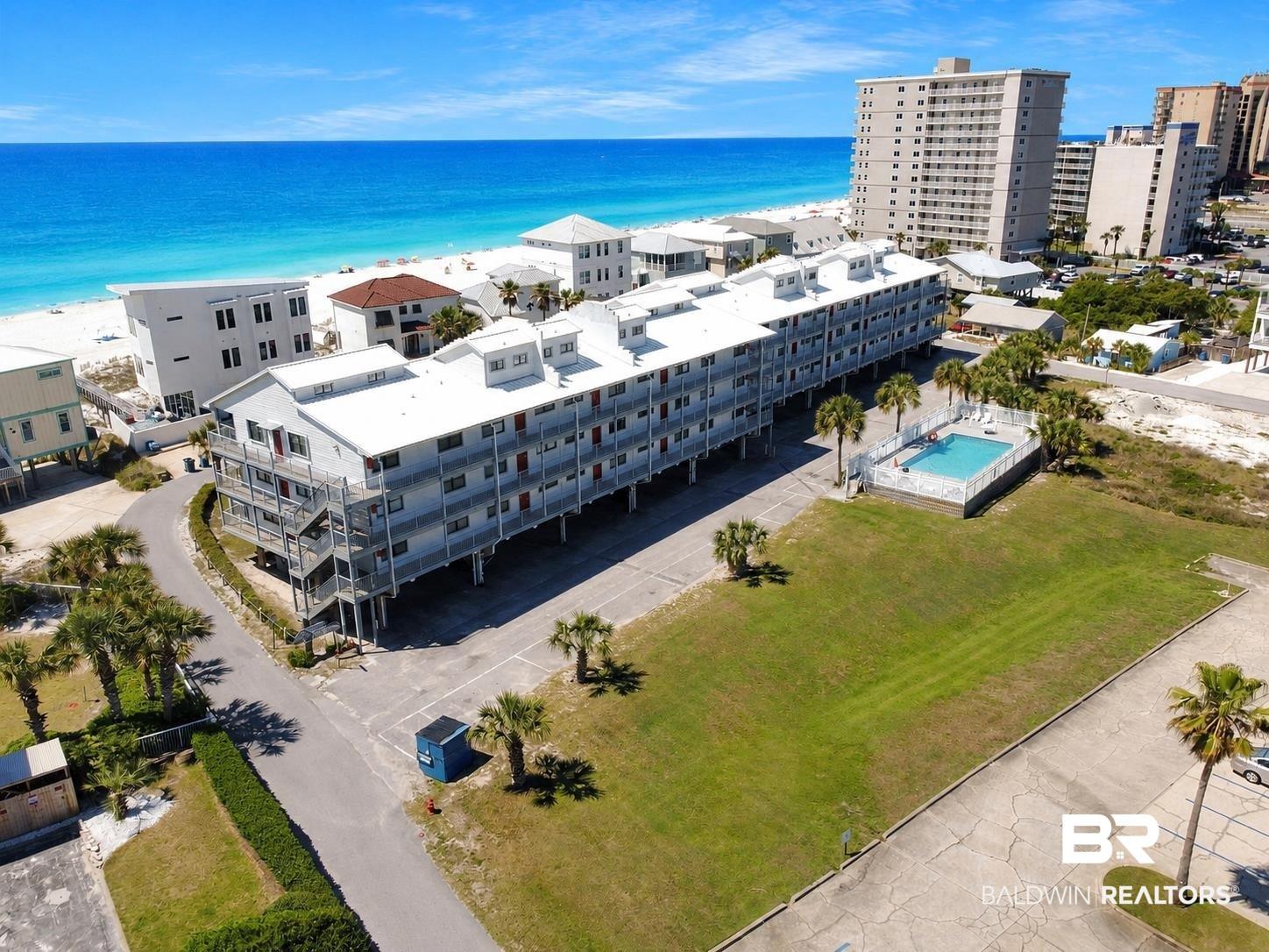 Image 2: Coastal multi-story building featuring multiple balconies, an outdoor swimming pool, and direct access to a white sand beach and turquoise water