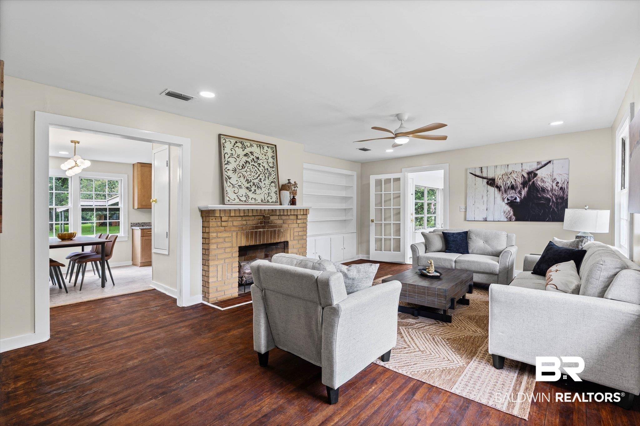 Image 2: Living area featuring rich wood-finish flooring, a brick fireplace, built-in shelving, and white French doors
