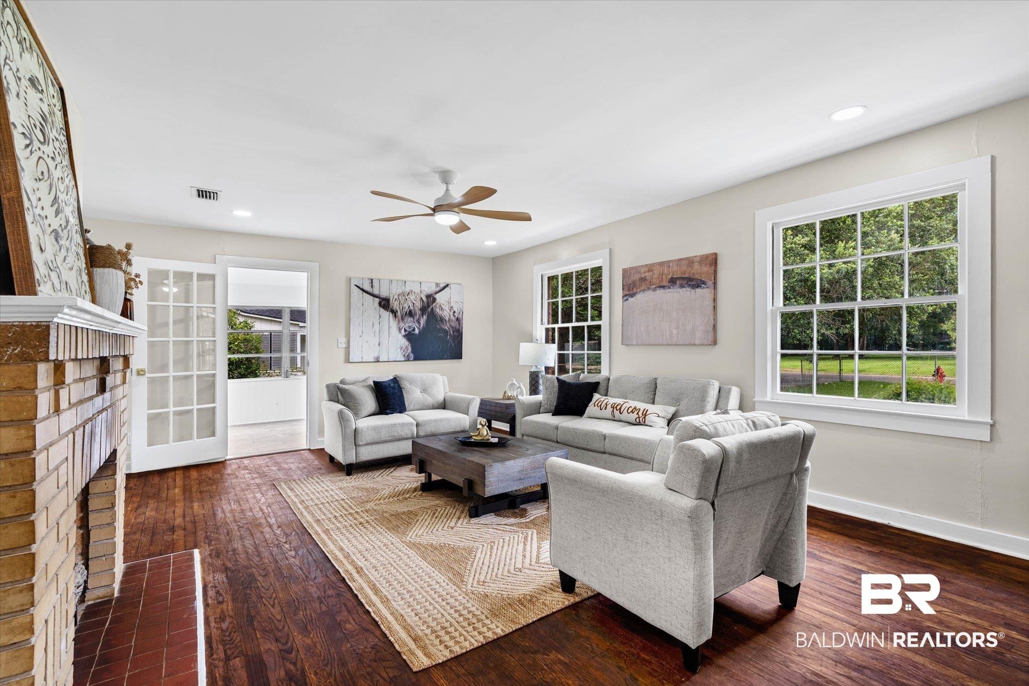 Image 4: Spacious living area featuring wood-finish flooring, a brick fireplace, French doors, recessed lighting, and a ceiling fan