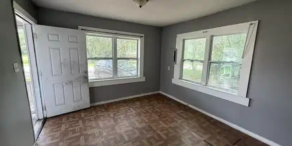 Image 3: Room featuring patterned wood-finish flooring, two large windows with white trim, and a flush-mount ceiling light fixture