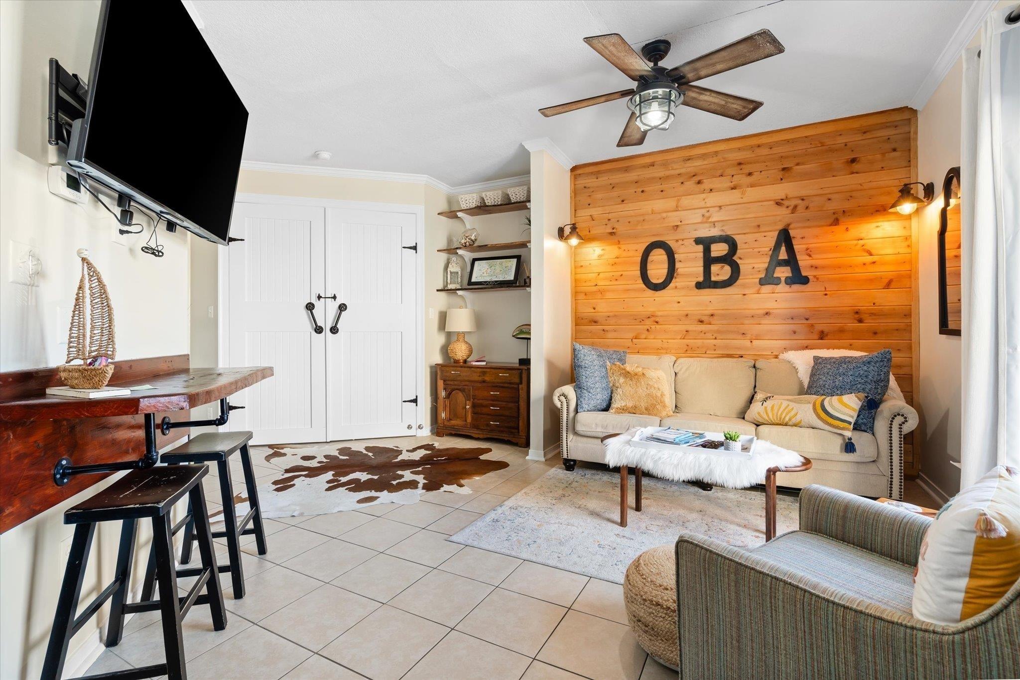 Image 3: Living room featuring ornamental molding, wood walls, ceiling fan, and light tile patterned floors