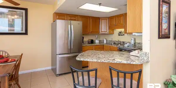 Image 4: Kitchen featuring granite countertops, wood cabinetry, stainless steel appliances, and a breakfast bar with seating
