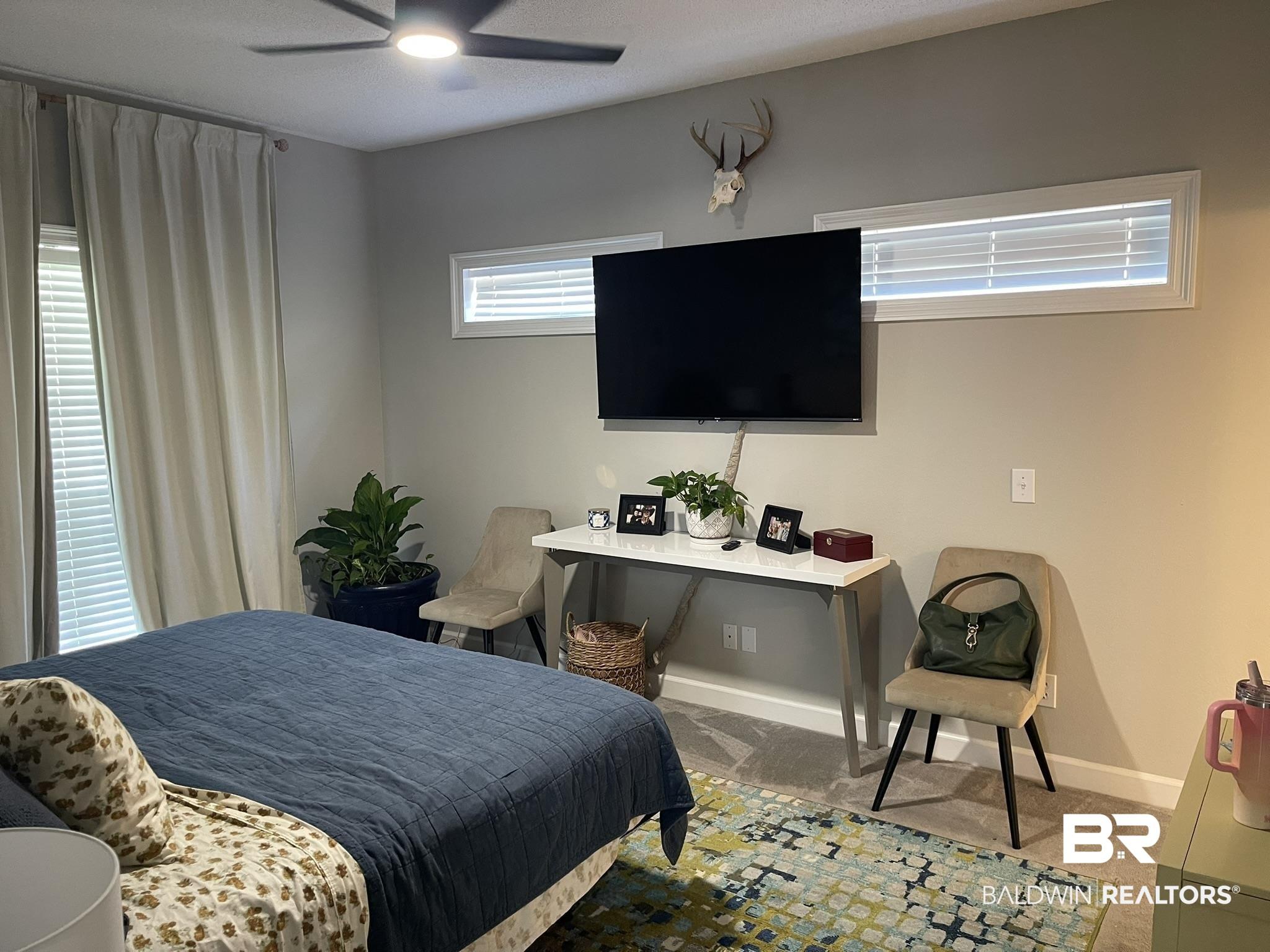 Image 3: Carpeted room featuring a ceiling fan, dual transom windows, and a built-in wall-mounted television