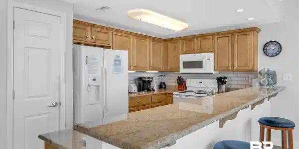 Image 4: Kitchen featuring a kitchen breakfast bar, white appliances, light stone counters, tasteful backsplash, and a peninsula