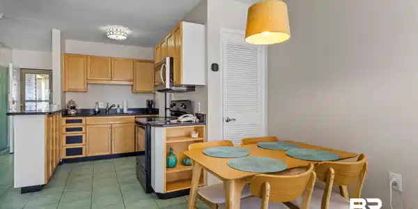 Image 4: Open-concept kitchen and dining area featuring wood-finish cabinetry, dark countertops, and integrated stainless steel appliances