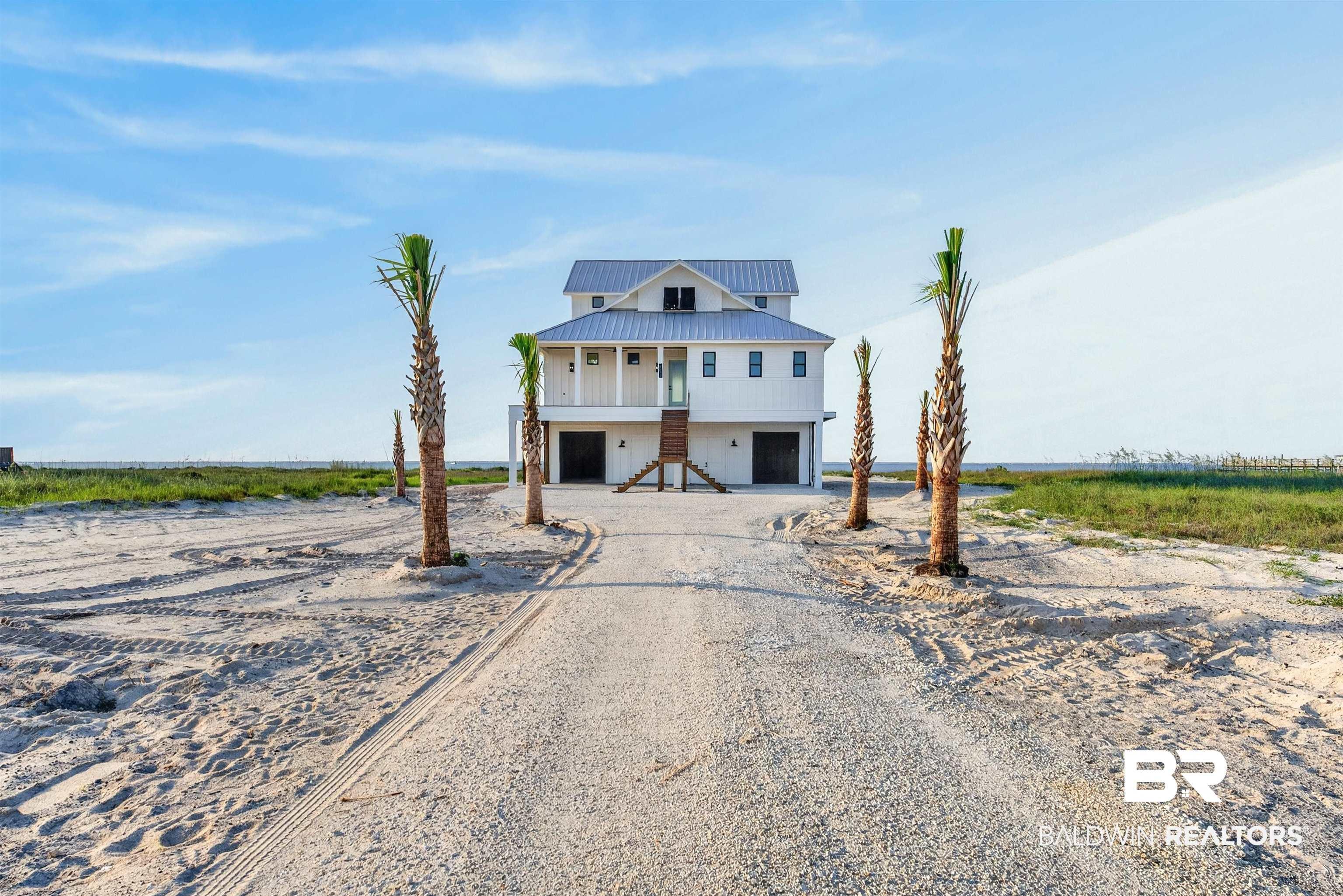 Image 2: Coastal home featuring a light-colored exterior, an elevated structure, and a metal roof