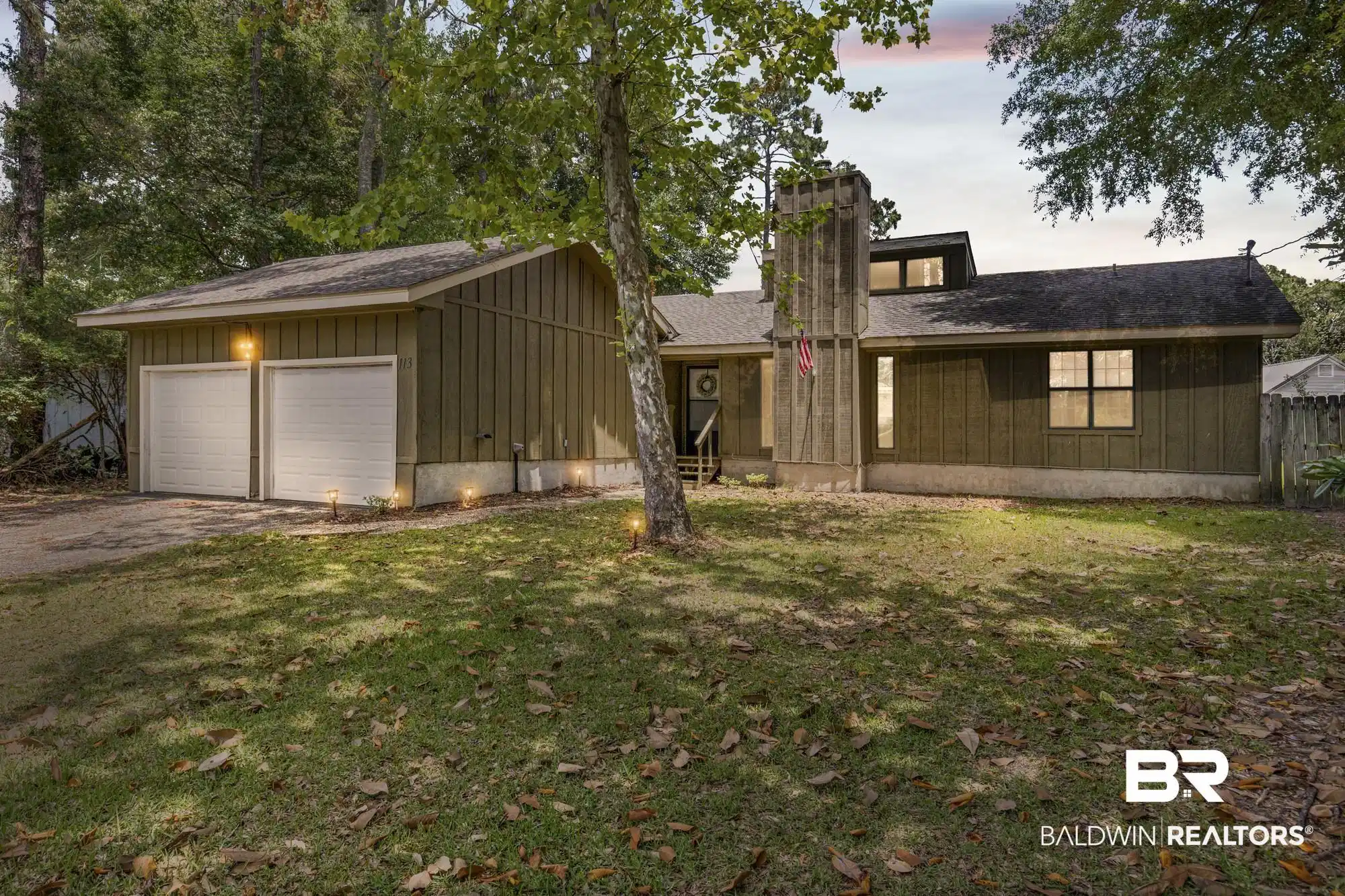 Image 1: Property exterior featuring a two-car garage, board and batten siding, a prominent chimney structure, multiple windows, and exterior lighting