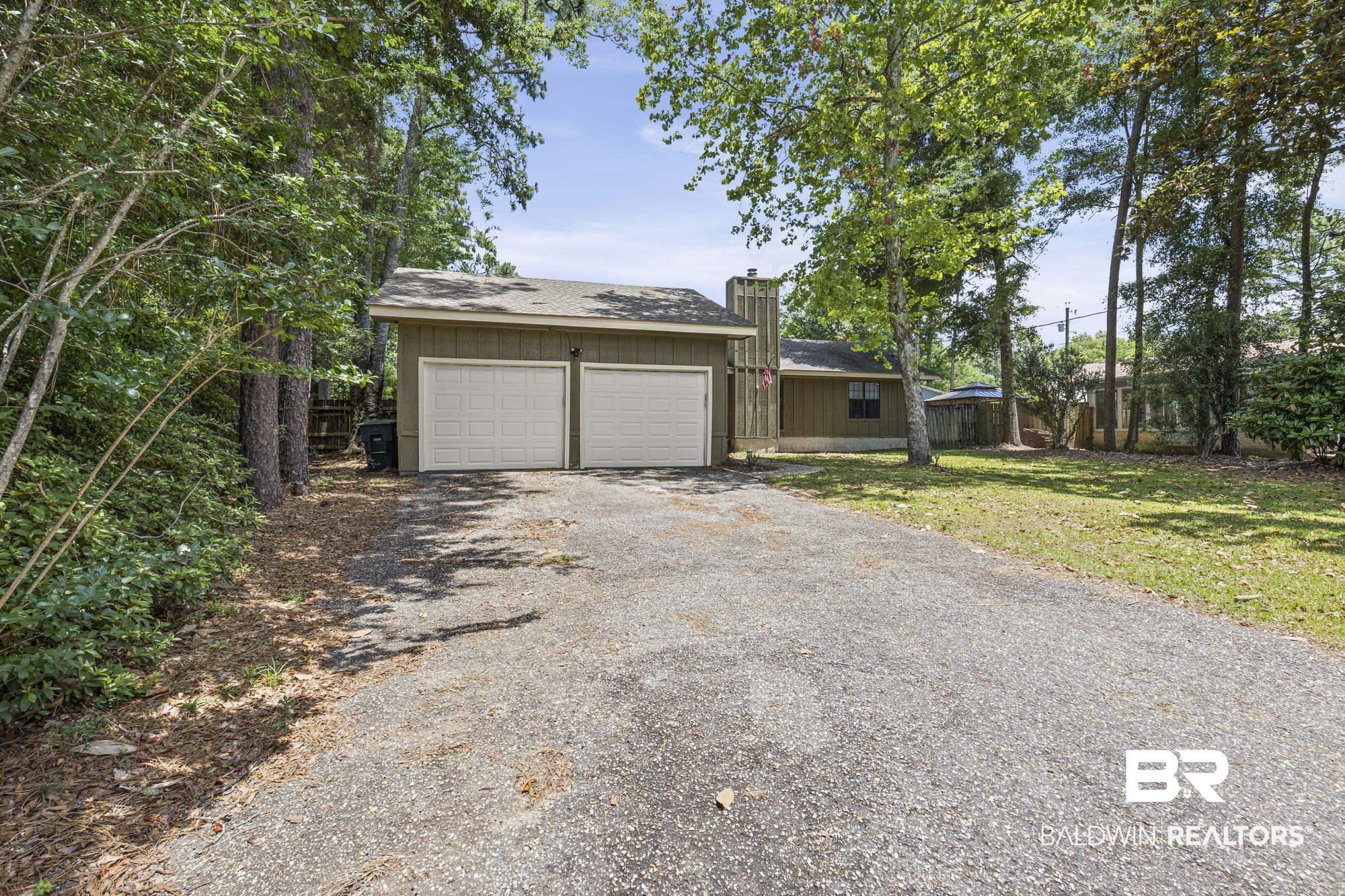 Image 2: Two-car garage with white panel doors and a shingled roof, set against a backdrop of mature trees and a gravel driveway