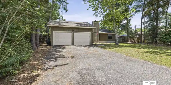 Image 2: Two-car garage with white panel doors and a shingled roof, set against a backdrop of mature trees and a gravel driveway