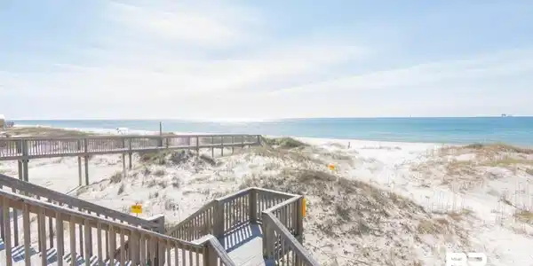 Image 2: Wood-finish boardwalk access to a white sand beach with natural dunes and ocean water
