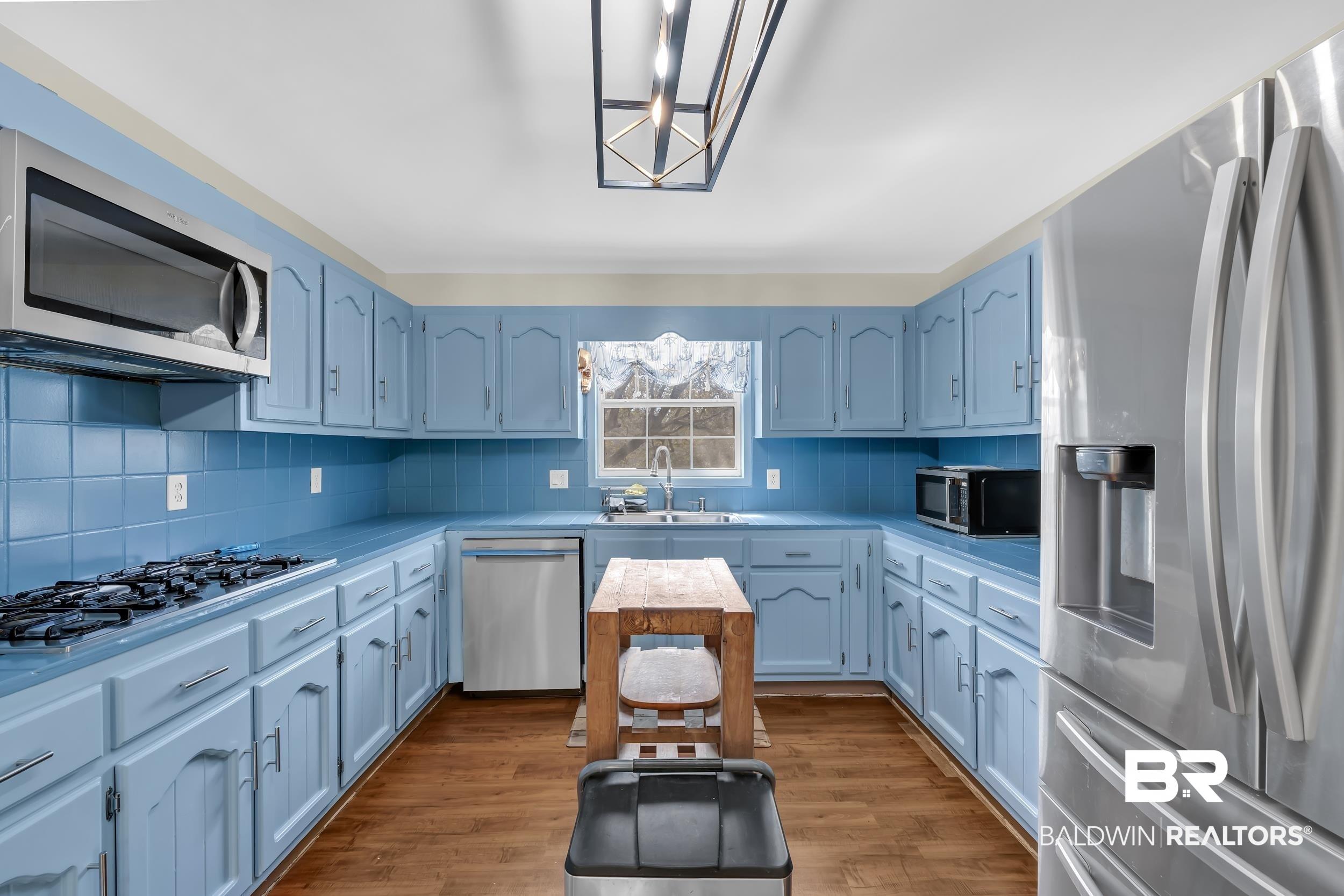 Image 3: Kitchen featuring stainless steel appliances, light countertops, light wood finished floors, and decorative backsplash
