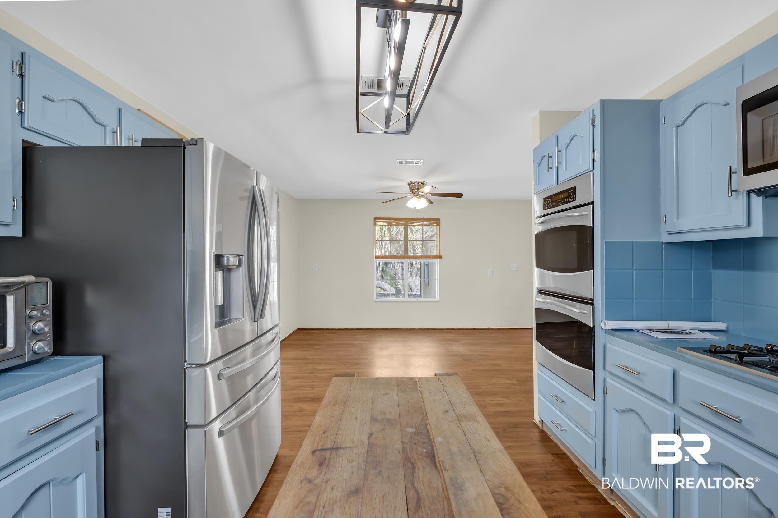 Image 4: Kitchen featuring blue cabinets, stainless steel appliances, light wood-type flooring, light countertops, and suspended lighting
