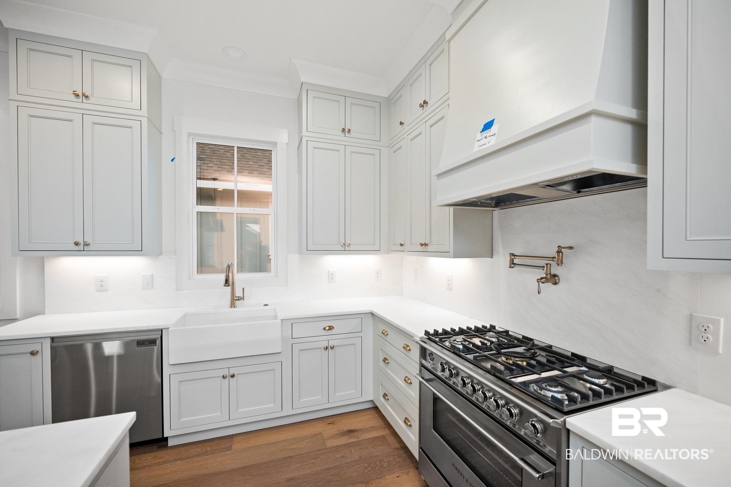 Image 4: Spacious kitchen featuring light gray cabinetry, under-cabinet lighting, a farmhouse sink, stainless steel appliances, and wood-finish flooring