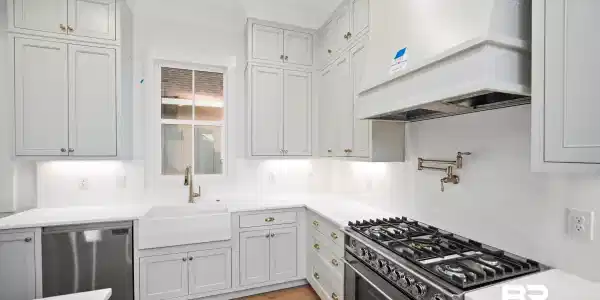 Image 4: Spacious kitchen featuring light gray cabinetry, under-cabinet lighting, a farmhouse sink, stainless steel appliances, and wood-finish flooring