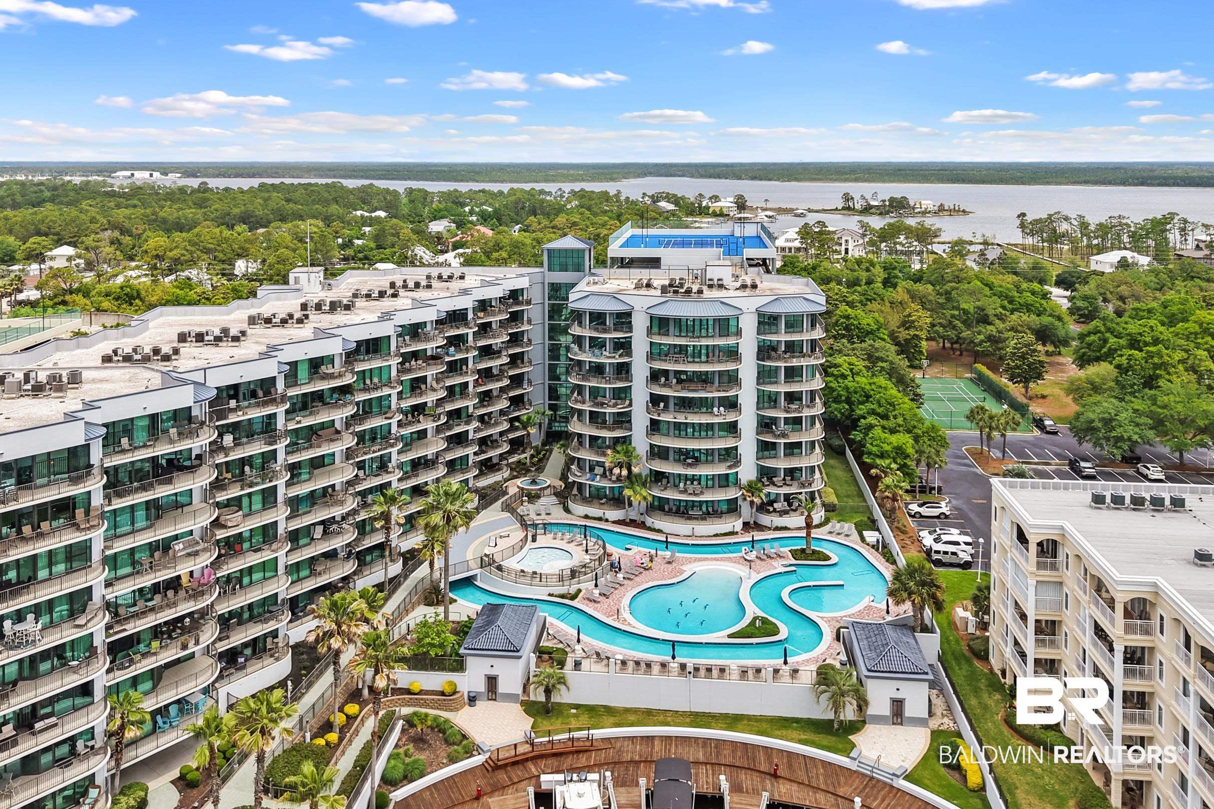 Image 2: Aerial view of a pool, a large body of water, apartment complex, and a tree filled landscape