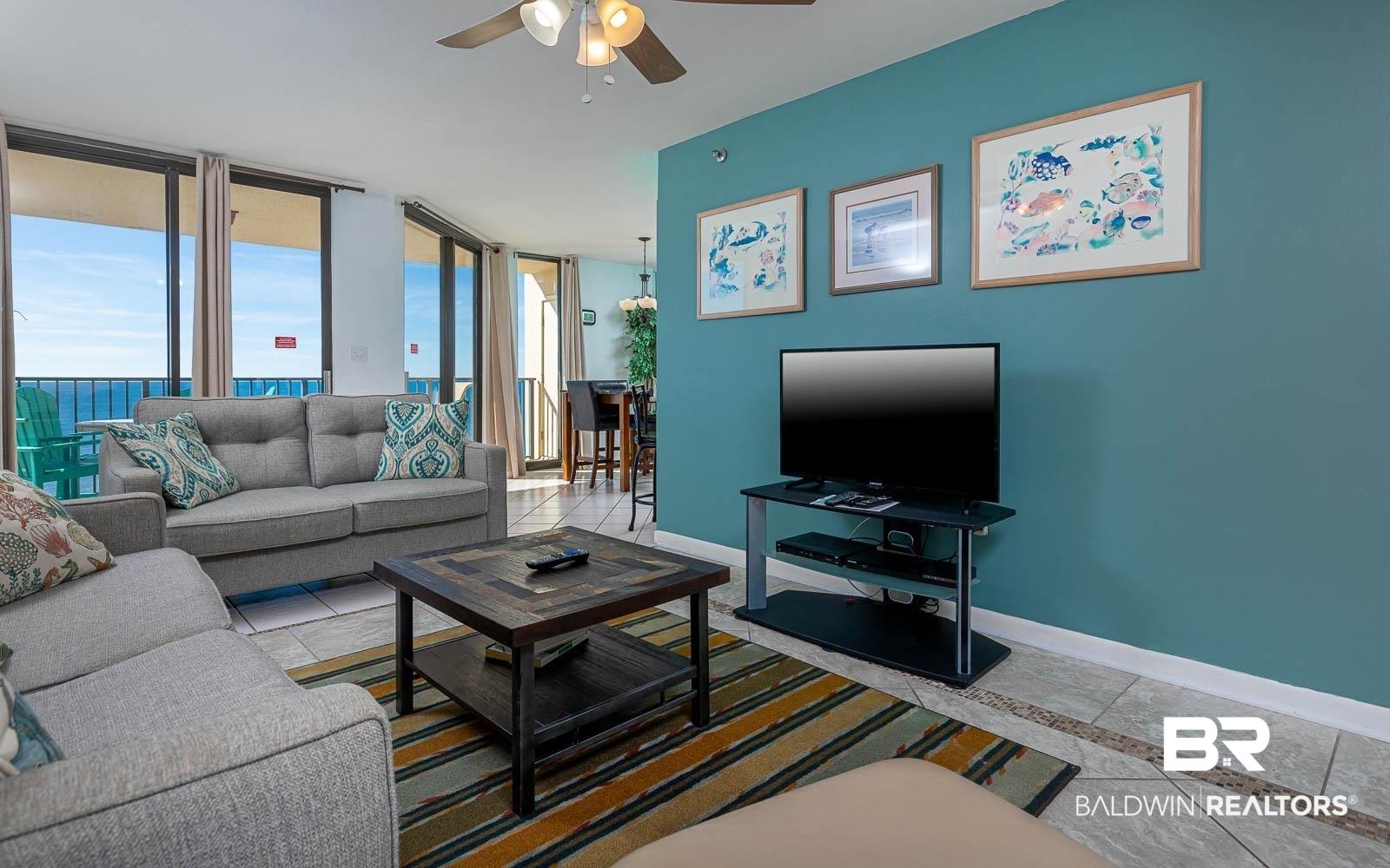 Image 3: Living area with light tile patterned flooring, expansive windows, and a ceiling fan