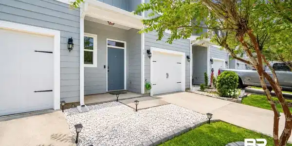 Image 2: Contemporary townhome exterior featuring light blue siding, a covered entry, and an integrated single-car garage with decorative hardware