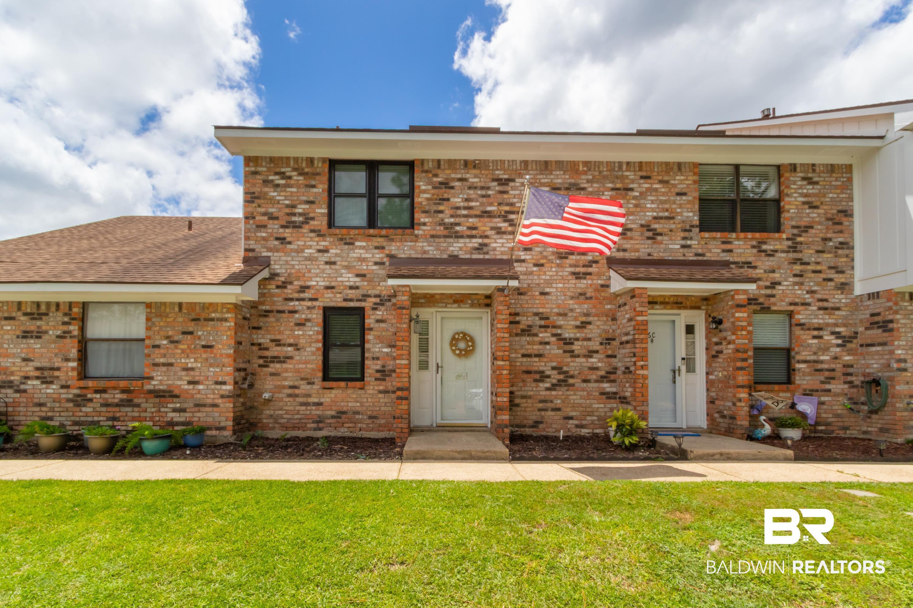 Image 2: Brick exterior featuring a brown shingle roof, white entry doors, and dark-framed windows