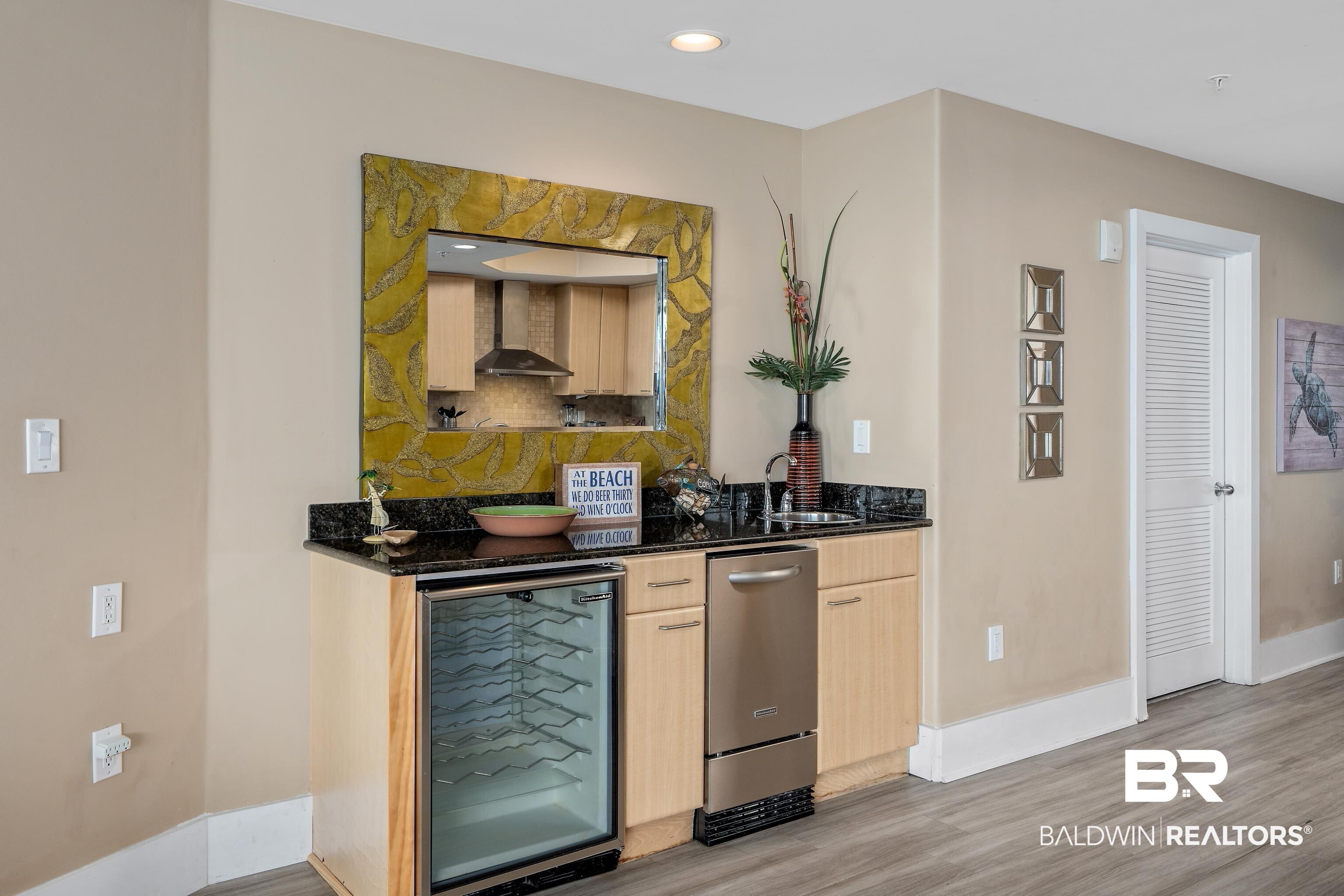 Image 4: Bar with wall chimney exhaust hood, wine cooler, sink, light brown cabinetry, and light hardwood / wood-style floors