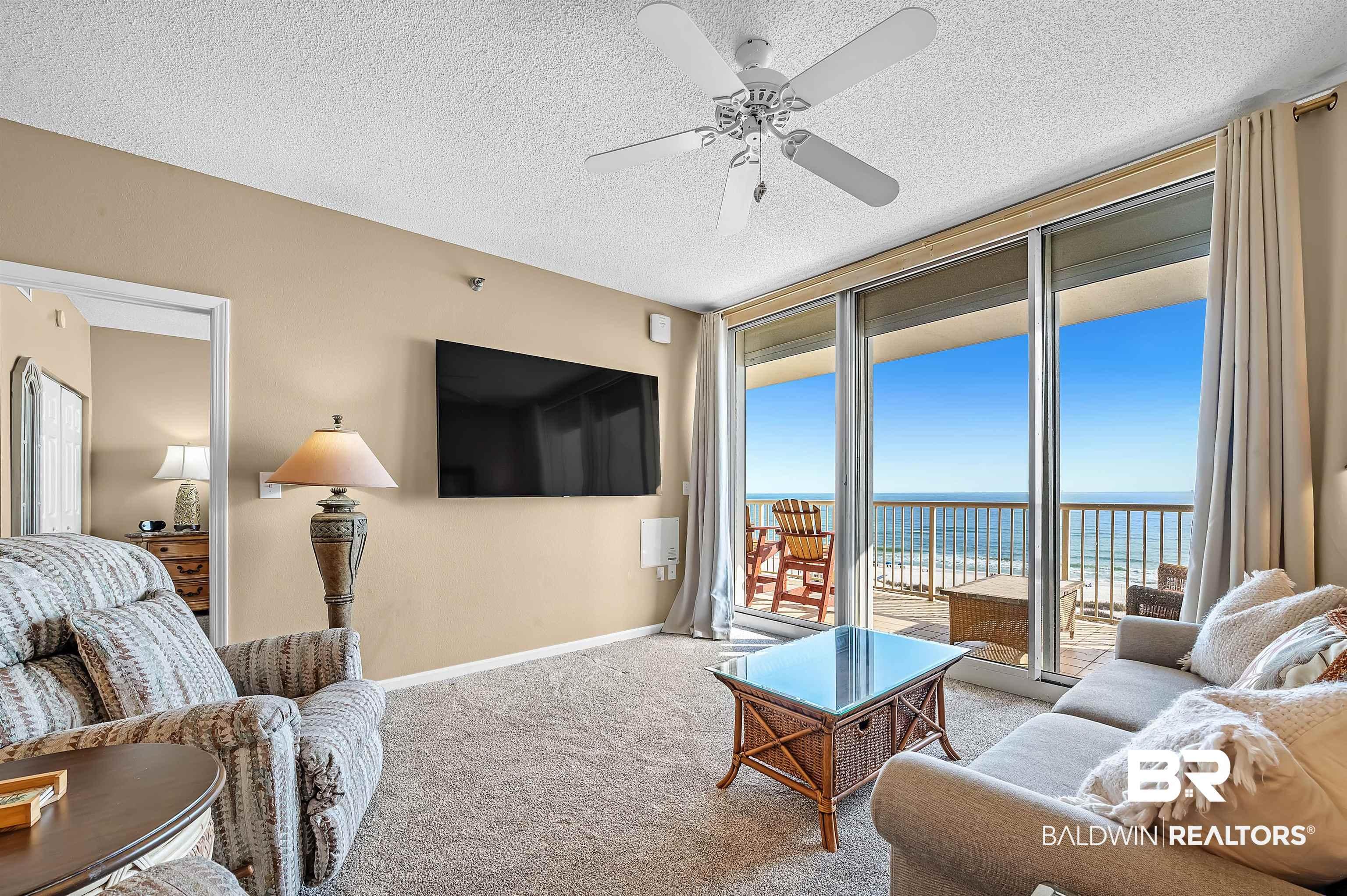 Image 4: Living area featuring a ceiling fan, a textured ceiling, carpet, a wall of windows, and baseboards