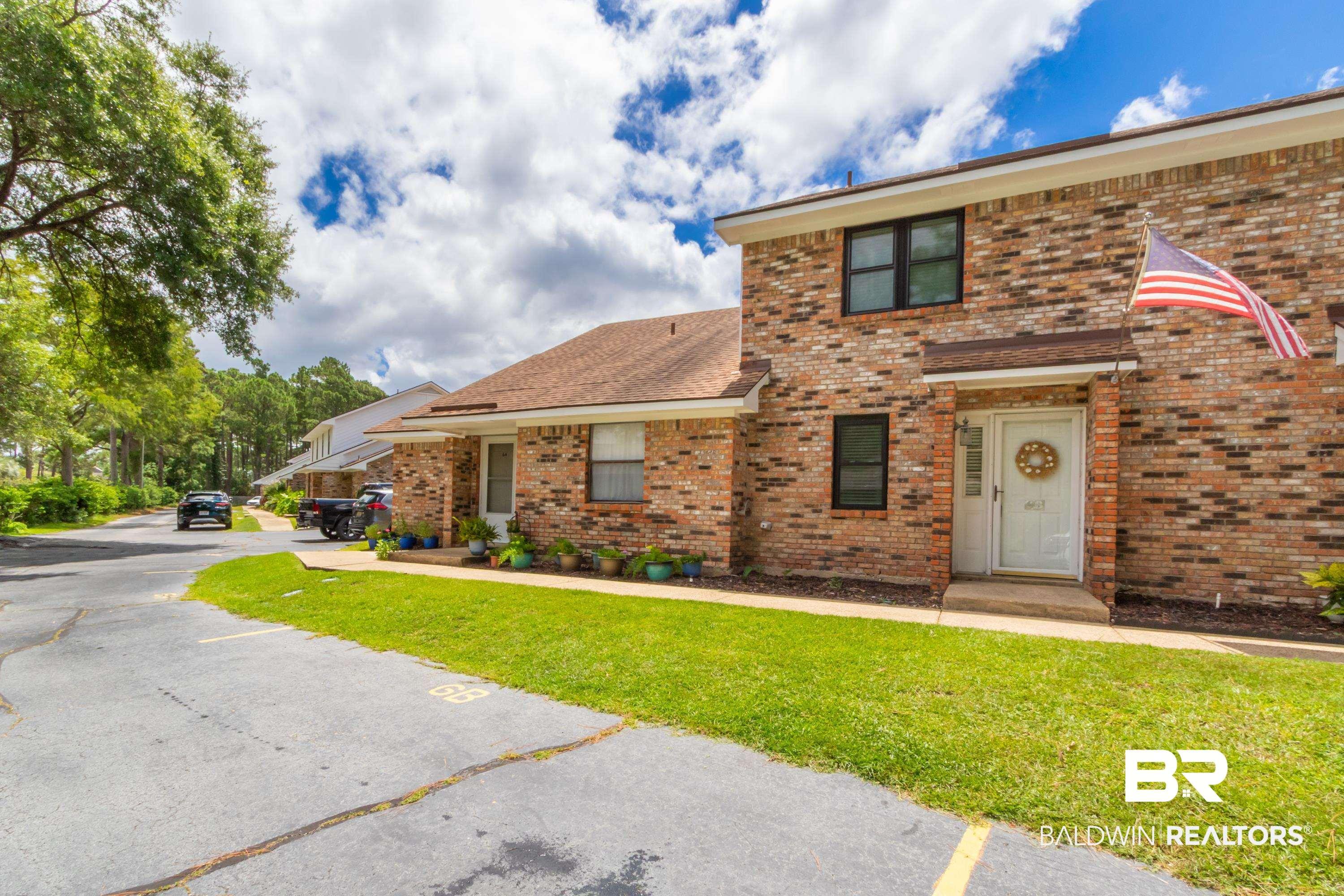 Image 3: Brick exterior townhome with a covered entryway, a white front door, and black-framed windows, surrounded by green lawn