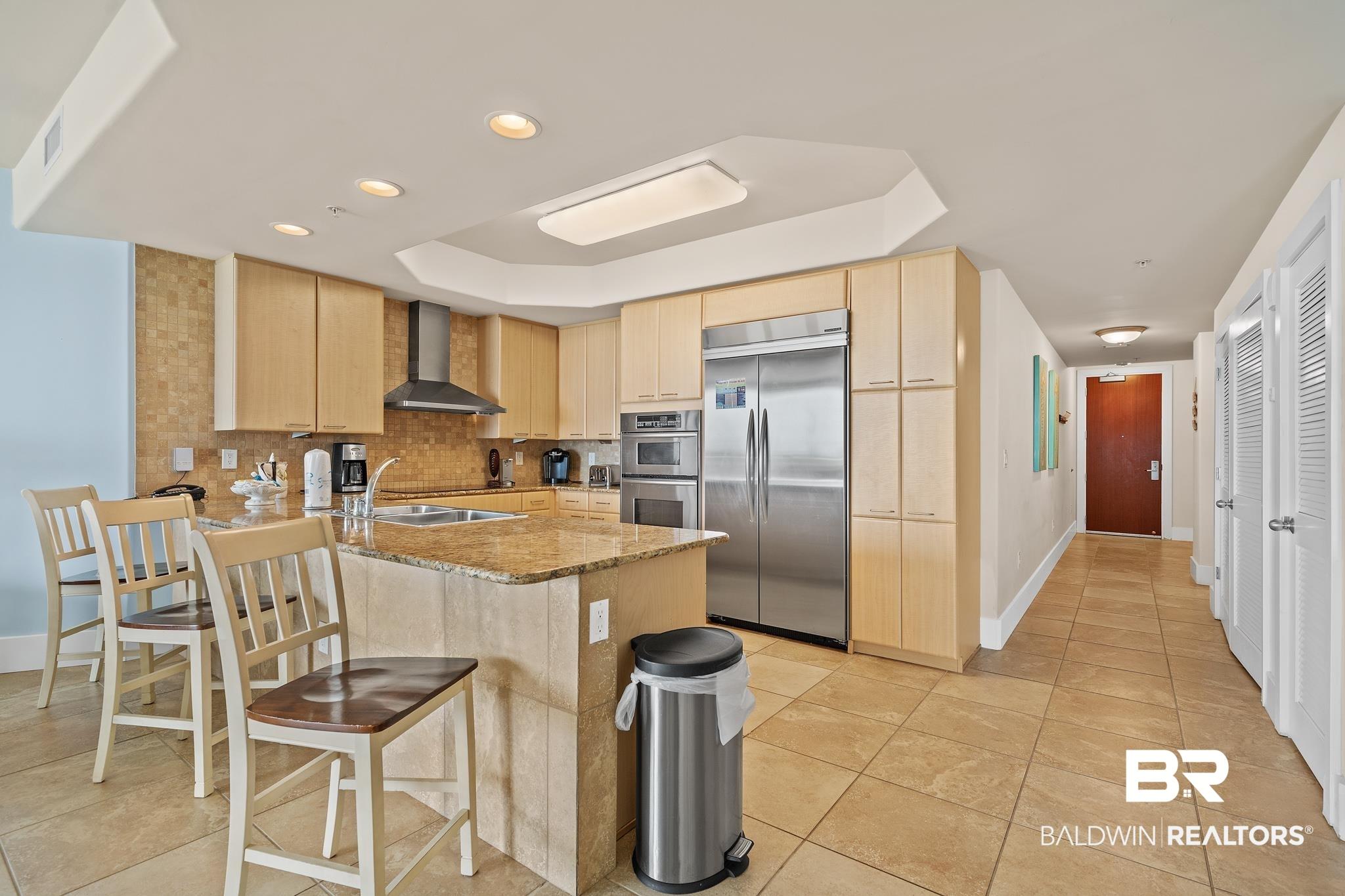 Image 4: Kitchen with stainless steel appliances, wall chimney exhaust hood, a tray ceiling, a peninsula, and recessed lighting
