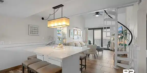 Image 2: Open-concept living space with a kitchen island featuring a light-toned countertop, a linear pendant light fixture, and tile flooring