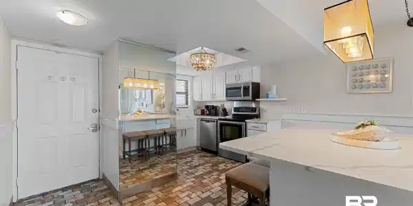 Image 4: Kitchen featuring white cabinetry, stainless steel appliances, a white island with a countertop, and brick-patterned flooring