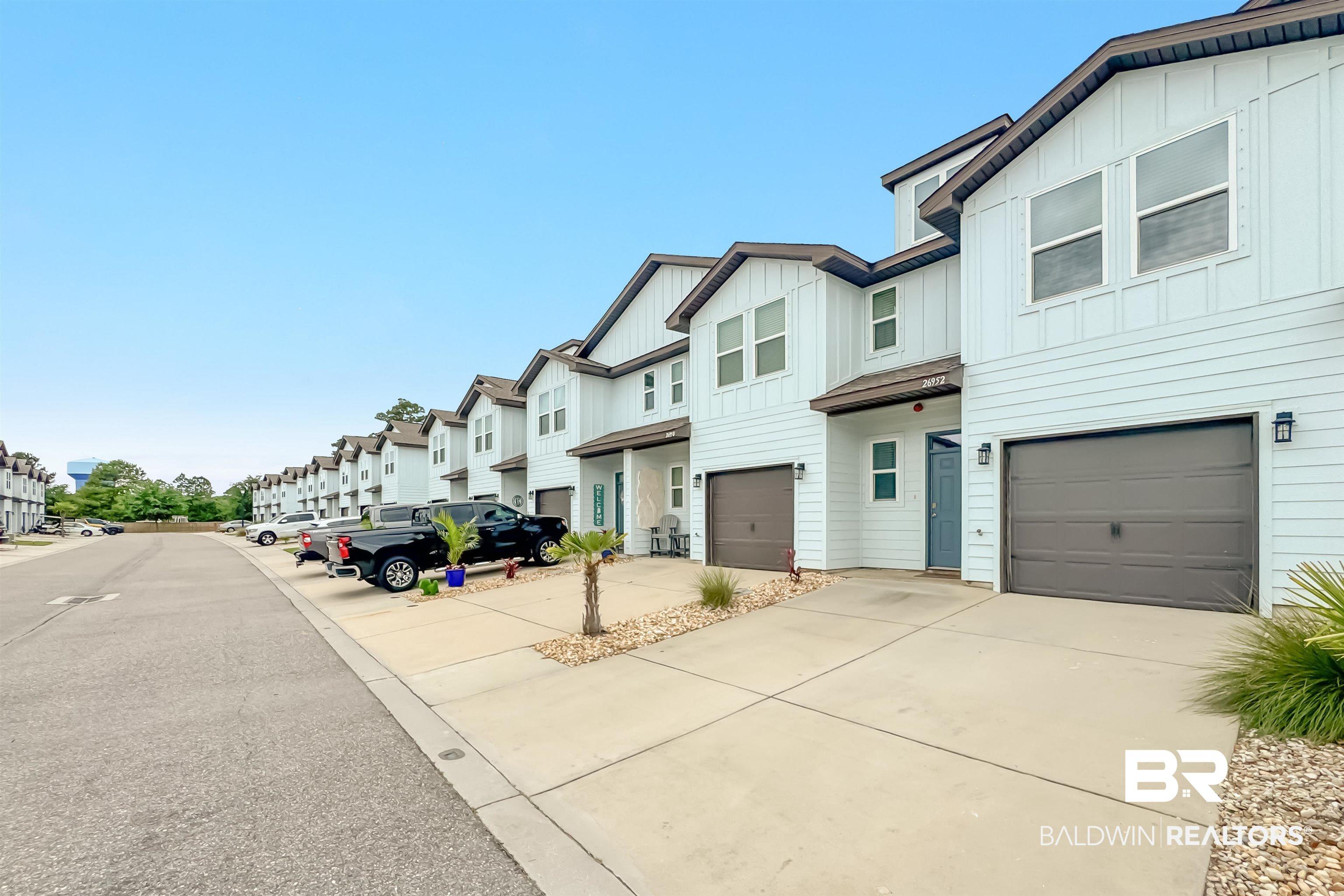 Image 2: Contemporary townhome exterior featuring light-colored siding, a dark brown roofline, and an integrated garage with a dark brown door