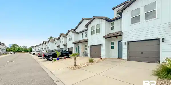 Image 2: Contemporary townhome exterior featuring light-colored siding, a dark brown roofline, and an integrated garage with a dark brown door