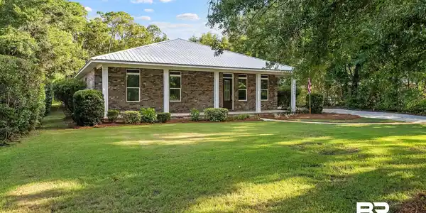 Image 4: Brick exterior with a white metal roof and a covered front porch featuring four white columns
